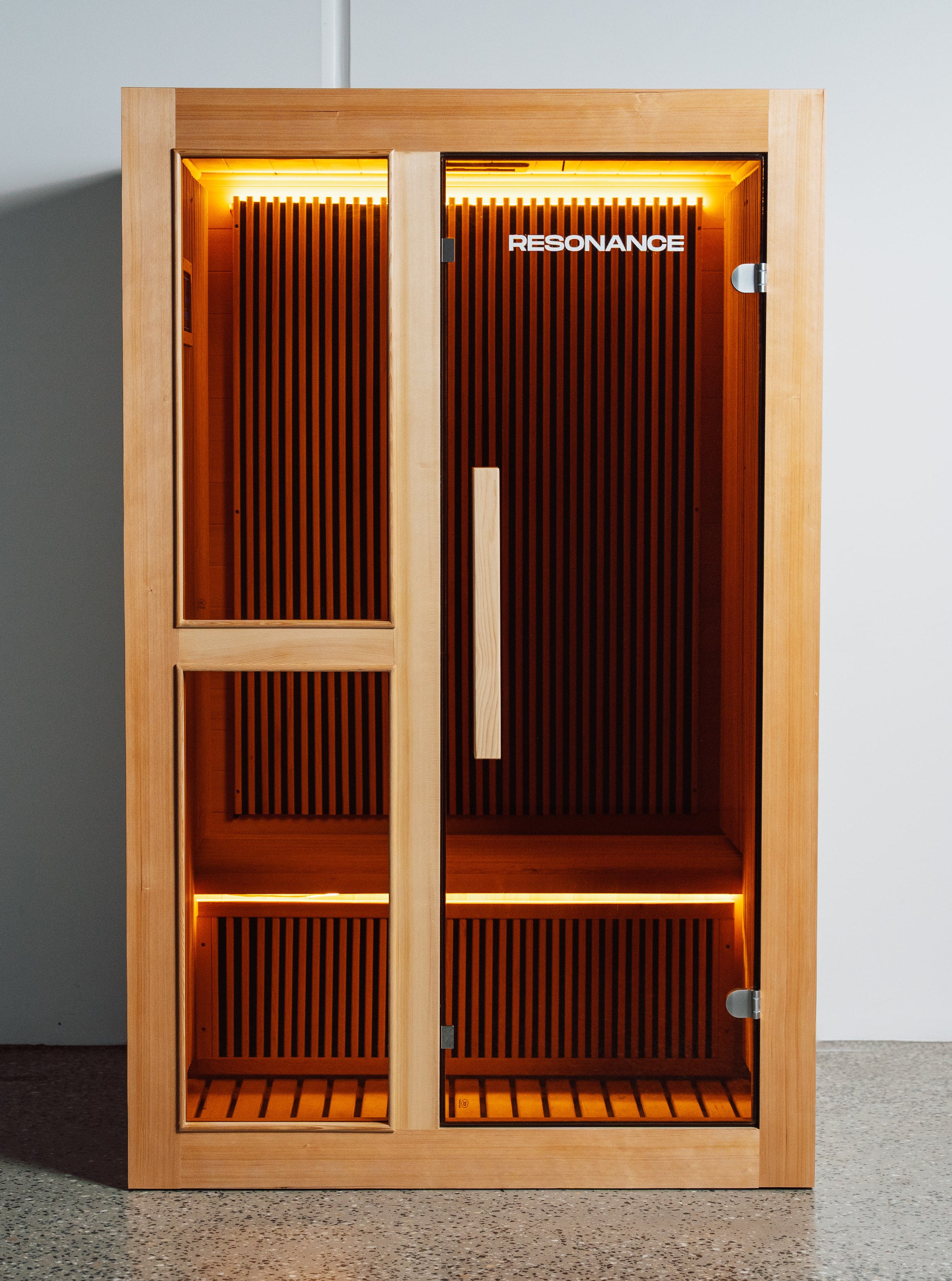 Resonance Recovery Pod exterior — 2-person infrared sauna with glass doors and cedar frame, warmly lit