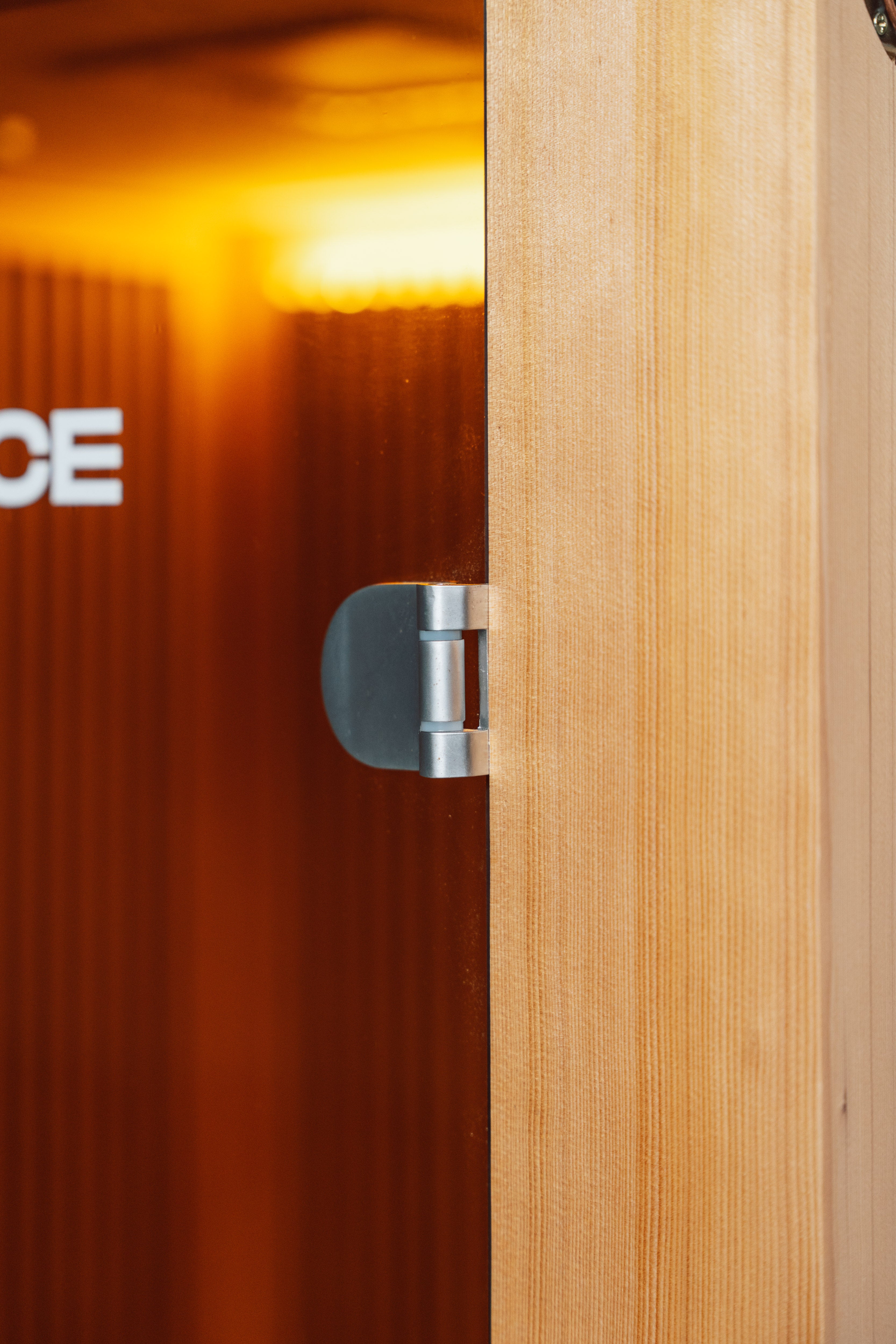 Recovery Pod sauna door hinge close-up — stainless steel hinge on natural cedar door frame with Resonance branding visible inside