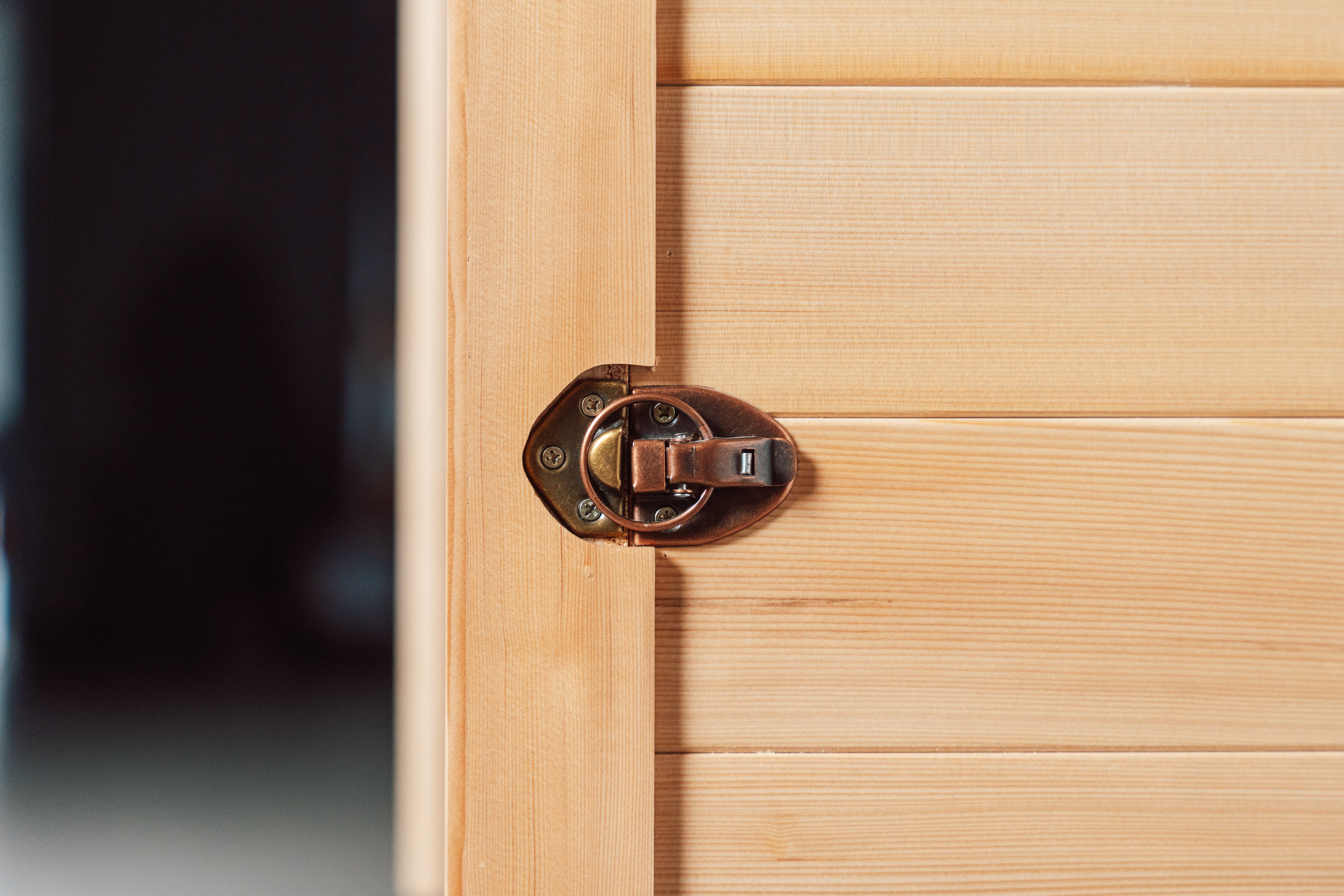 Recovery Pod sauna door latch close-up — bronze barrel bolt hardware on natural Canadian Hemlock cedar panel