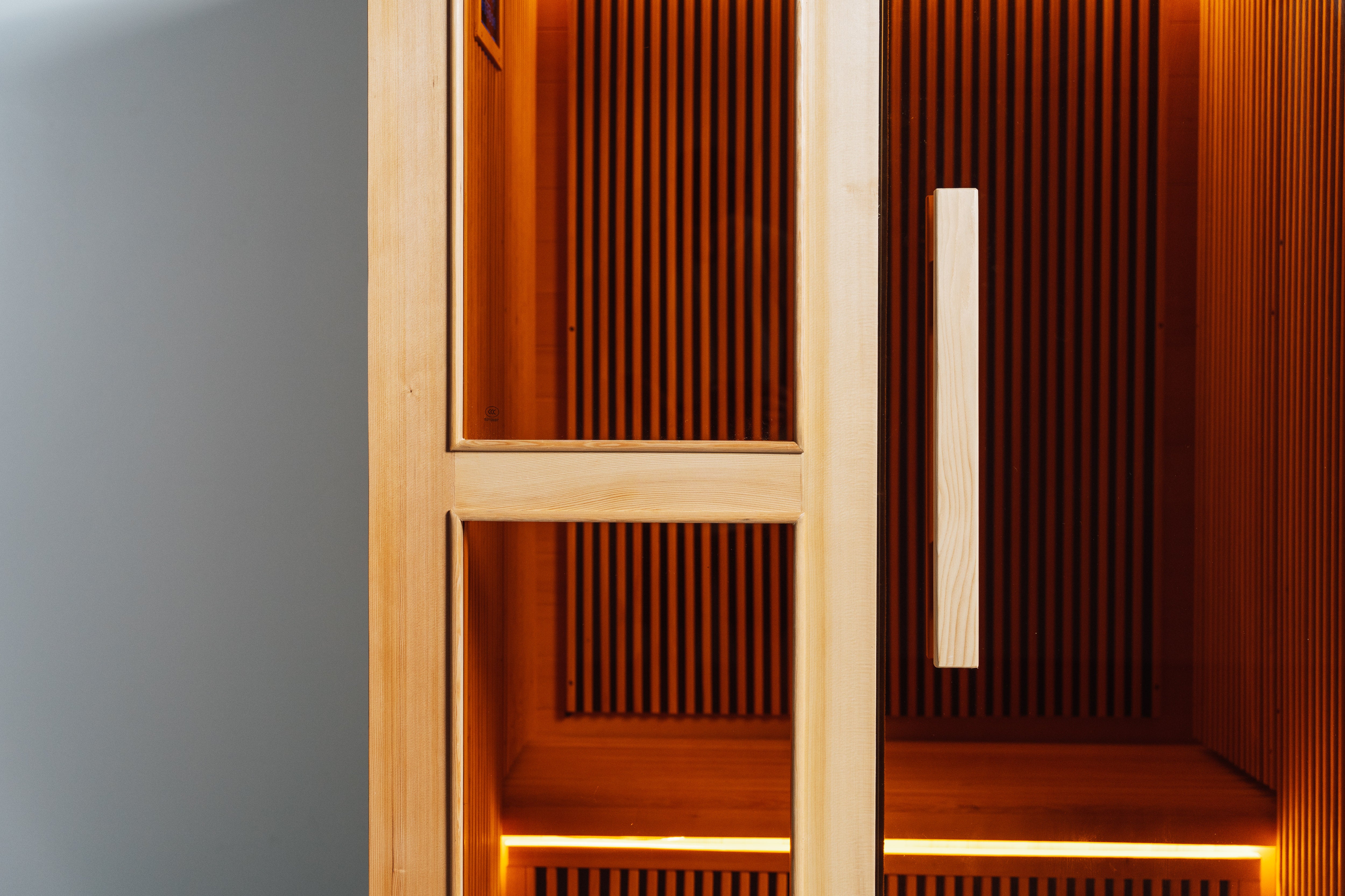 Recovery Pod glass door close-up — cedar frame and wooden handle with warm infrared lit interior visible through full glass panel